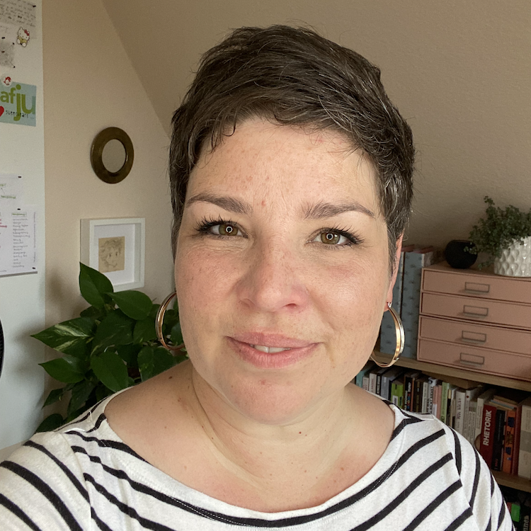 Autorin Maren Gutzmann Die Autorin lächelt in die Kamera, im Hintergrund sind Teile ihres Büros zu erkennen. Sie hat kurze, dunkle Haare und trägt ein schwarz-weißes Streifenshirt und Kreolen in den Ohren.